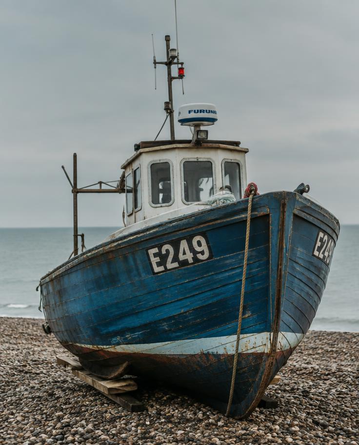Weathered blue fishing boat on a pebble shore